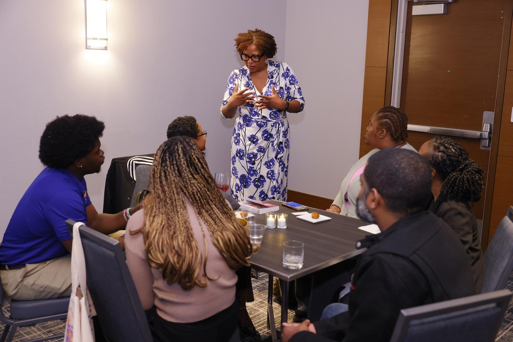 Tayari Jones standing and chatting with #AWP25 HBCU fellows seated at a reception table
